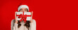 © Prostock-studio - Happy woman wearing santa hat holds Xmas gift box before face on red studio backdrop, looking at camera hiding behind Chistmas present. Festive sales and surprises, copy space