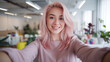 © Tom - A cheerful young Asian woman with pink hair smiles as she takes a selfie in a bright, modern office with plants in the background.