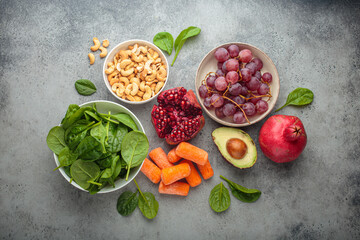 Assortment of healthy potassium rich foods including cashews, grapes, avocado, pomegranate, baby carrot and spinach placed on a gray background, a balanced diet for wellness