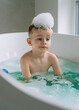 © Elena - The boy enjoys a relaxing bath in the spacious bathtub with turquoise water, the spacious bathroom is flooded with sunlight thanks to large floor-to-ceiling windows.