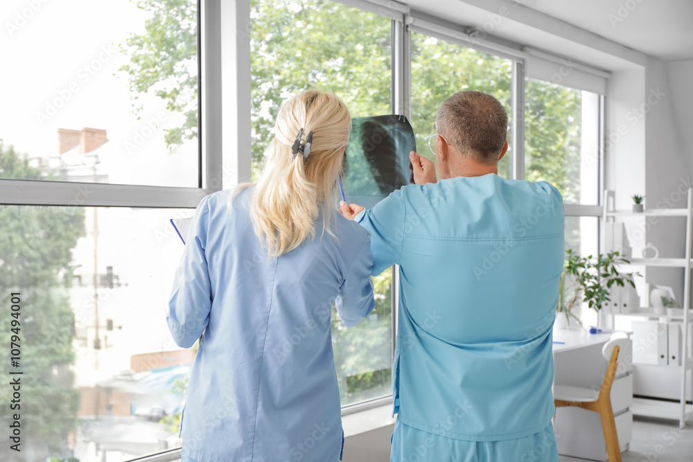 Mature doctors studying x-ray image of lungs in clinic, back view