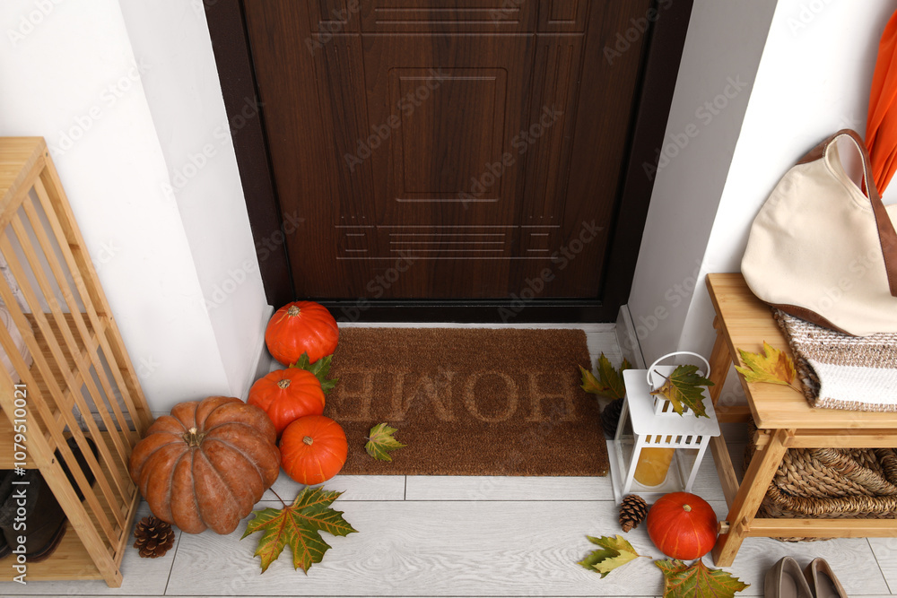 Doormat with pumpkins, lantern and autumn leaves in hallway