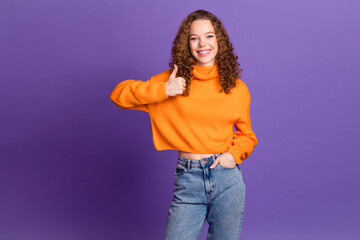 Wall Mural - Portrait of pretty young girl show thumb up wear orange sweater isolated on purple color background