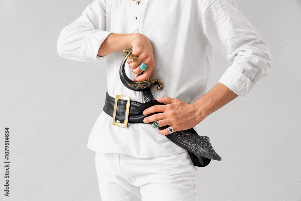 Young pirate with saber on light background, closeup