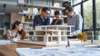 © Mas - Group of architects discussing architectural models with shop drawing paper on office table