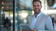© Орися Зигмунд - Smiling Caucasian man in a light suit holding a tablet, exuding professionalism and confidence in a modern office environment.