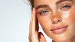 © M - Close-up portrait of a young woman with freckles and glowing skin, gently touching her face, natural beauty concept