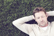 © peopleimages.com - Man, relax and sleeping on grass outdoor for resting, afternoon nap and exhausted in backyard. Calm person, face and dreaming on lawn at park with fatigue, tired and break with top view in nature