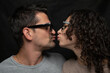 © Marco Taliani - A young man and a young woman wearing sunglasses are about to kiss each other on the mouth against a black background