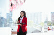 © Witoon - Asian businesswoman in red suit holding tablet while standing in city street