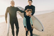 © Marko Geber - Grandfather and grandson in wetsuits carrying surfboards on the beach