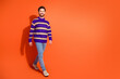 © deagreez - Confident bearded man in a striped sweater walking across orange backdrop, exuding style and positivity