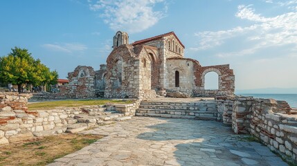 Wall Mural - Ruins of an ancient stone church on a sunny day with a clear blue sky and a body of water in the background.