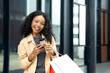 © Jestercine - Happy woman holding shopping bags, a credit card, and a smartphone outdoors, representing online shopping and retail satisfaction.