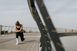 © BGStock72 - A young woman stretches during her morning workout on a modern city bridge under a clear blue sky