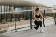 © BGStock72 - A young woman exercises outdoors at sunset, stretching her legs near a modern building in an urban environment, embracing an active lifestyle