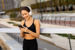 © BGStock72 - Woman enjoys her workout while listening to music outside a modern building on a sunny day in the city park