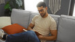© Krakenimages.com - Young man with beard reading book on couch in modern living room interior, wearing glasses and casual outfit, enjoying relaxed leisure time at home.