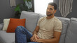 © Krakenimages.com - Young hispanic man with beard relaxing indoors on a comfortable sofa in a modern apartment living room, exuding an attractive and composed presence.