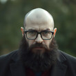 © patypixie - Un hombre calvo, con lentes y barba larga que mira hacia el frente con molestia