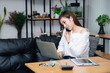 © skarie - Businesswoman talking on phone working on laptop in modern office. Sharing good business news. Woman working on laptop at office while talking on phone.