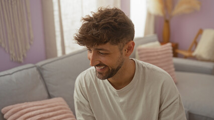 Wall Mural - Young man smiling indoors in a cozy living room setting with pastel decor and plush cushions, showcasing a relaxed home atmosphere