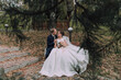 © Vasil - A bride and groom are sitting on a bench in a park. The bride is wearing a white dress and the groom is wearing a suit. They are holding hands and smiling at the camera. Scene is happy and romantic