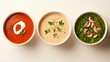 © Rashedul - Top view of three bowls of soup in a line: tomato with cream swirl, creamy mushroom with mushroom slices, and green vegetable with fresh herbs, on a minimalist background