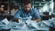 © Dulemegapixel - A man appears overwhelmed as he stares at a multitude of papers scattered across a cluttered office desk, highlighting the stress and chaos of a busy workload.