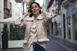 © javgutierrez - Brunette model wearing a beige vest with white fur and a satin shirt posing on a city street