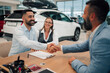 © Zamrznuti tonovi - Content pair shaking hands with dealer after closing car deal.