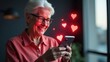 © Helga P-A. - A smiling senior woman looks at her smartphone, surrounded by glowing red hearts, suggesting online romance or positive social media interactions. Concept of senior dating and online connection.