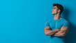© sun - Young muscular man in a blue shirt standing confidently against a vibrant turquoise background with arms crossed, showcasing strength and determination in a dynamic pose.