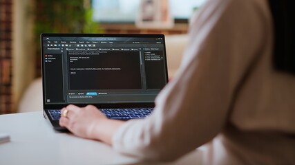 Asian female programmer works on coding software in a home office setup, typing code on a laptop. IT expert uses digital tools for multitasking, software development and app development. Camera B.