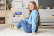 © Pixel-Shot - Young woman holding mobile phone with smart home security system control panel in room
