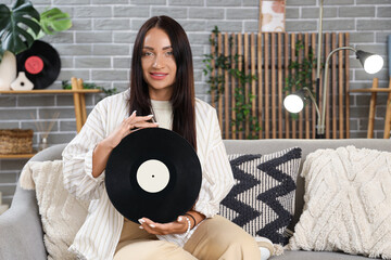 Wall Mural - Young woman with vinyl disk for record player sitting on sofa at home