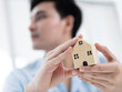 © M21Perfect - Real estate investment insights a man examines a miniature house indoor setting lifestyle concept contemporary viewpoint