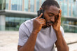 © Юлия Завалишина - Sad tired lonely disappointed African man alone talking on smartphone on city street outdoor. Unhappy person making answering call by cellphone experiencing grief getting bad news. Stressed man