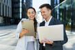 © muse studio - Business Professionals Collaborate on a Tablet and Laptop Outside a Modern Office Building During the Day