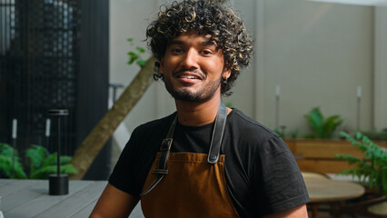 Happy joyful Latino American ethnic man male smiling cafe worker in apron guy waiter cleaner barista portrait small business owner employee looking at camera smile outside town. Employment street food