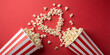 © Irma - Two striped popcorn buckets spilling popcorn into a heart shape on a vibrant red background, Valentine's Day, the concept of love and romance