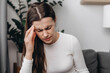 © Yura Yarema - Dizzy young female with headache or migraine pain suffering from vertigo while sitting on couch in living room at home, girl holding head with hand, health problem of brain or inner ear not balance