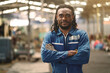 © KANGWANS - A man with dreadlocks is wearing a blue jumpsuit and is standing in a factory. He is smiling and looking directly at the camera