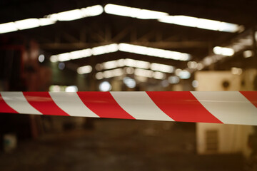 A red and white striped tape is hanging from the ceiling in a warehouse. The tape is long and is stretched out across the room. The warehouse is dimly lit, giving it a somewhat eerie atmosphere