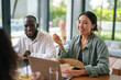 © Dorde - A smiling diverse group of young professionals enjoys a casual meal together in a sunlit modern office, engaging in conversation over laptops and fresh salads.