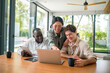 © Dorde - Three joyful young adults, a diverse group, engage in creative teamwork at a sleek laptop, in a well-lit, modern office, suggesting productivity and collaboration.
