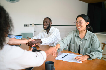 Wall Mural - A group of young male and female business professionals with varying ethnicities stack hands above a conference table, symbolizing unity and achievement in a corporate setting.