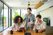 © Dorde - Three young adults, showing a mix of ethnicities, happily collaborate in a well-lit, contemporary office space, using digital tablets, papers, and a laptop.