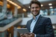 © Yuliia - young man in a suit smiling while using a digital tablet in a modern office.