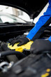© zphoto83 - Car maintenance technician inspecting engine components under the hood in a well-lit garage environment
